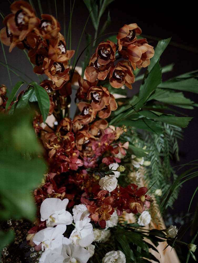 Textural close-up of tropical wedding florals with orchids, roses, and greenery.