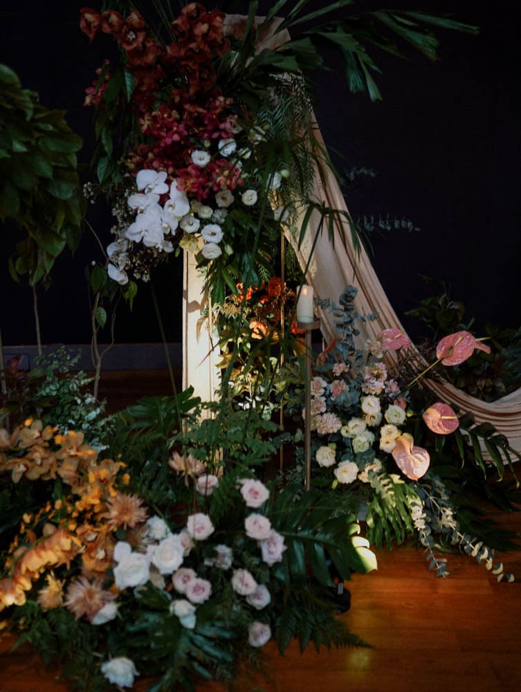Wedding stage backdrop at Capella with trailing orchids and greenery with low arrangements of roses and anthurium floral lush and drapes at Capella Hotel Singapore.