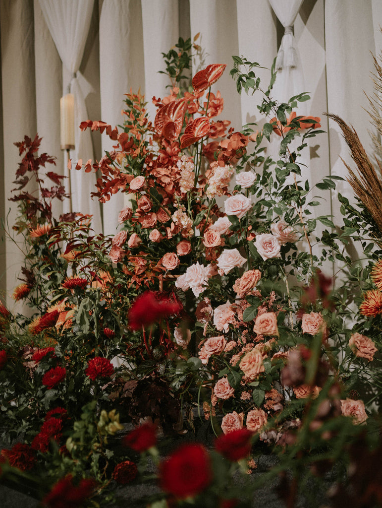 Layered autumn wedding florals in blush, red and green foliage arranged in a garden inspired stage design at Four Seasons Hotel Singapore