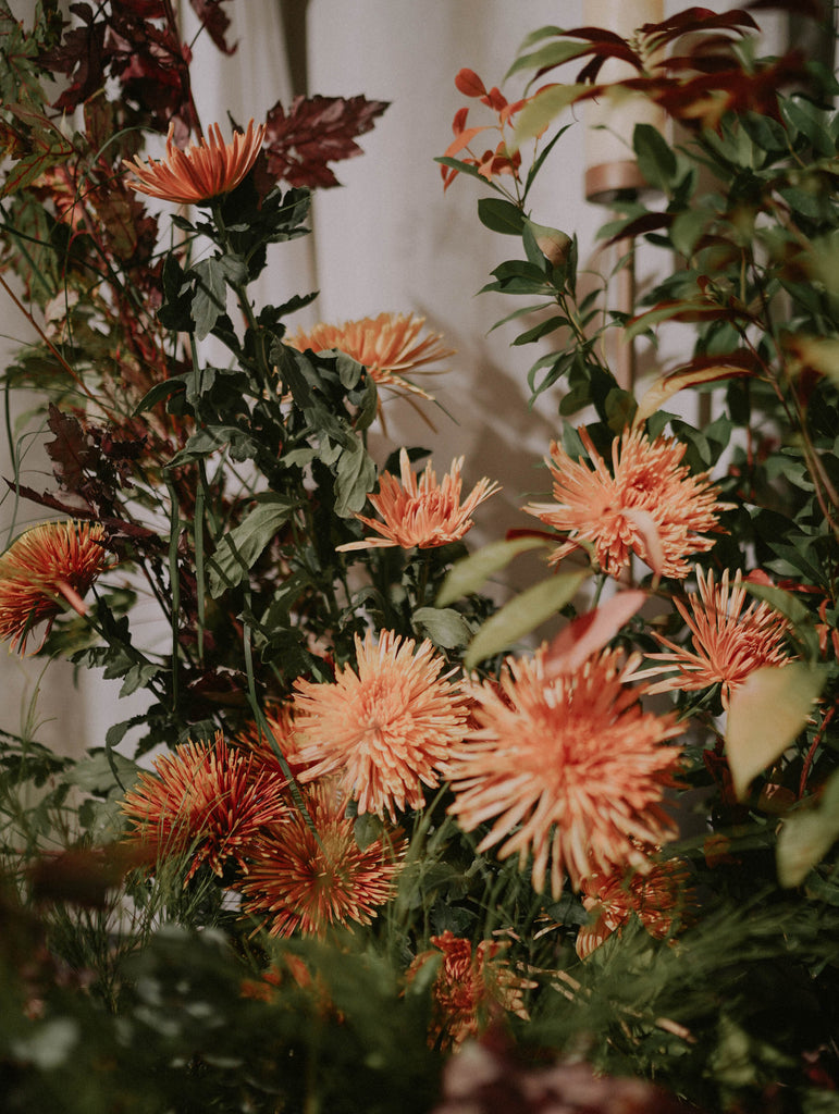 Textured arrangement of orange and terracotta blooms featuring bronze spider mum with brown dried foliage and layered greenery in warm tone wedding styling at Four Seasons Hotel Singapore