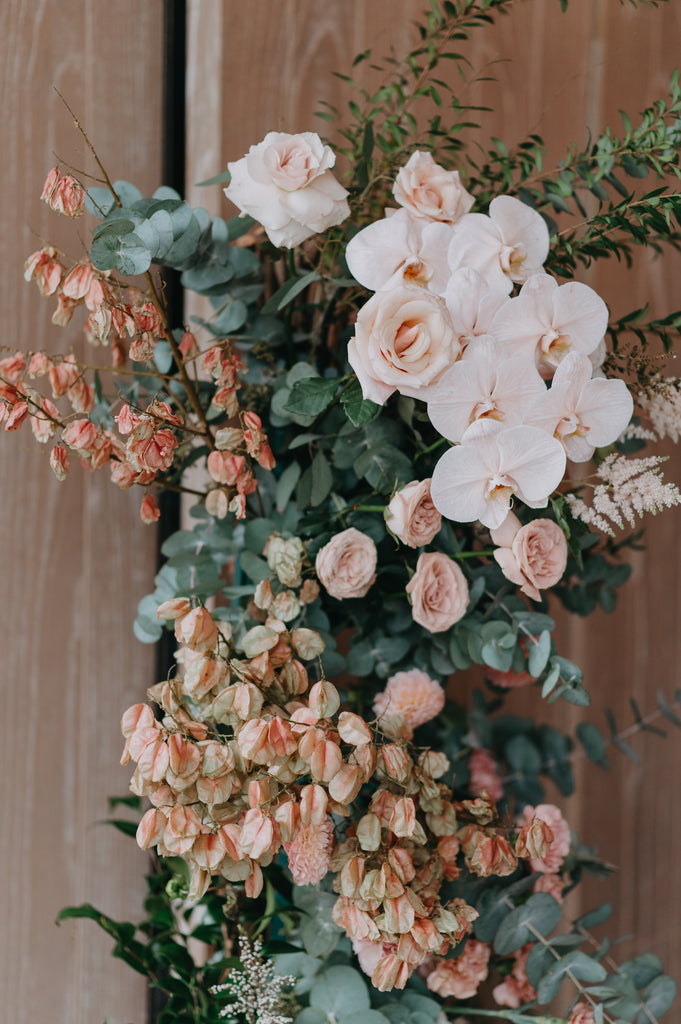 Closeup of warm tone floral arrangement with roses, orchids and greenery in a lush compact style at Andaz Singapore