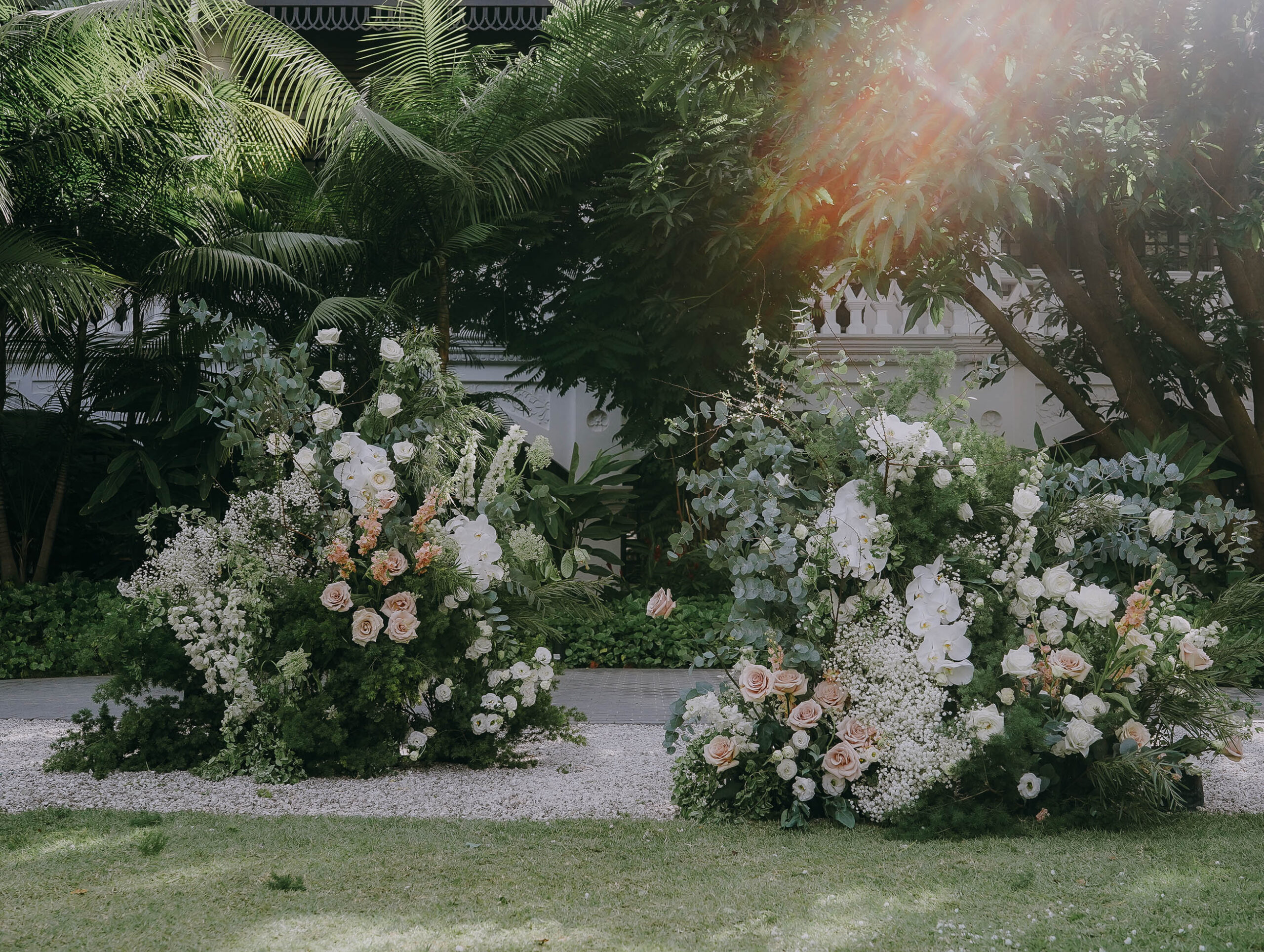 Garden wedding ceremony setup with deconstructed floral hill installation of white roses, blush roses, hydrangeas, and lush greenery forming a romantic backdrop at Raffles Hotel Singapore