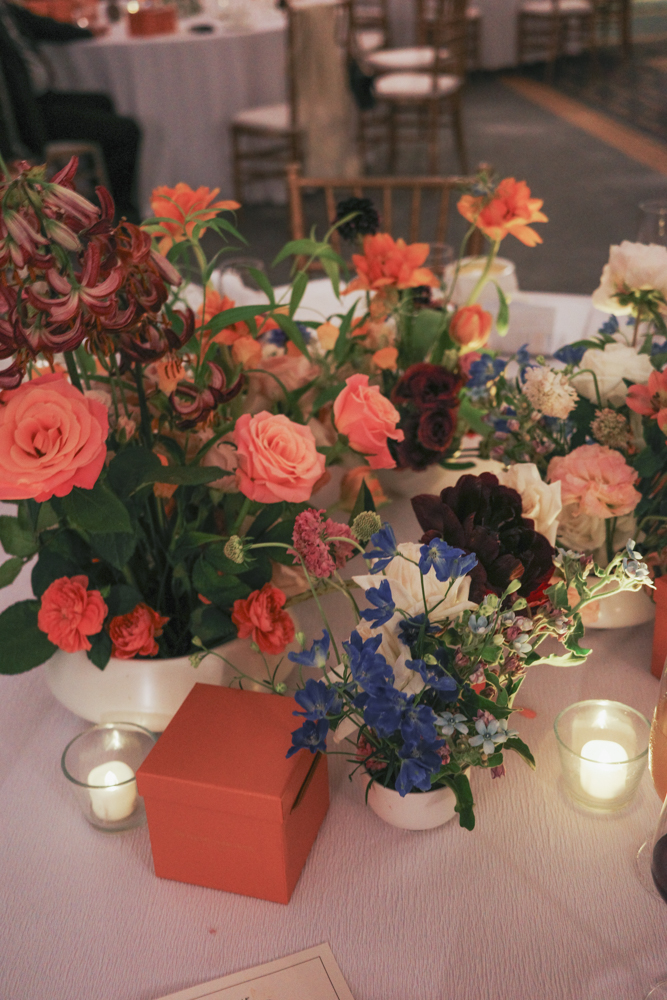 A detailed view of a vibrant centerpiece floral arrangement with orange, pink, white, and blue flowers, consisting of Delphiniums, Tiger Lilies, Roses, Carnations, Forget Me Nots and Tweedia with interesting textures at The Clifford Pier at The Fullerton Bay Hotel.