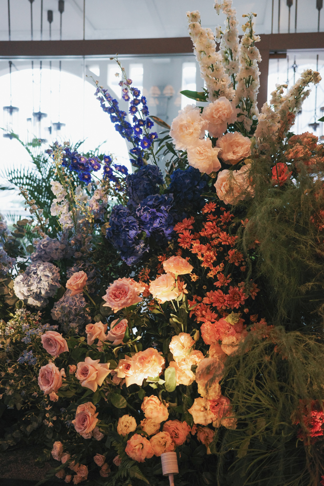 A close up of colorful wedding arch with tall and lush floral arrangement with blue, peach, cream, and green flowers and foliage, consisting of Roses, Hydrangeas, Delphiniums, Snapdragons, Peonies, Lisianthus and Dianthus creating a modern garden aesthetic at The Clifford Pier at The Fullerton Bay Hotel.
