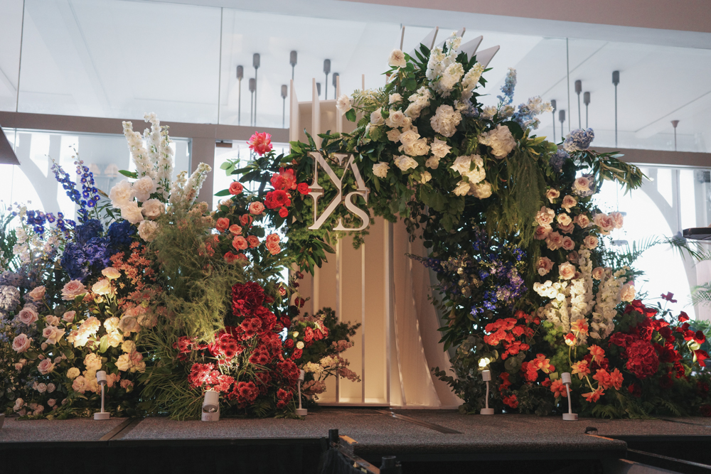 A colorful and modern floral archway or backdrop with red, white, blue, and green flowers and foliage, consisting of Roses, Hydrangeas, Delphiniums, Snapdragons, Peonies, Lisianthus, Dianthus and Orchids for a wedding decoration at The Clifford Pier at The Fullerton Bay Hotel.