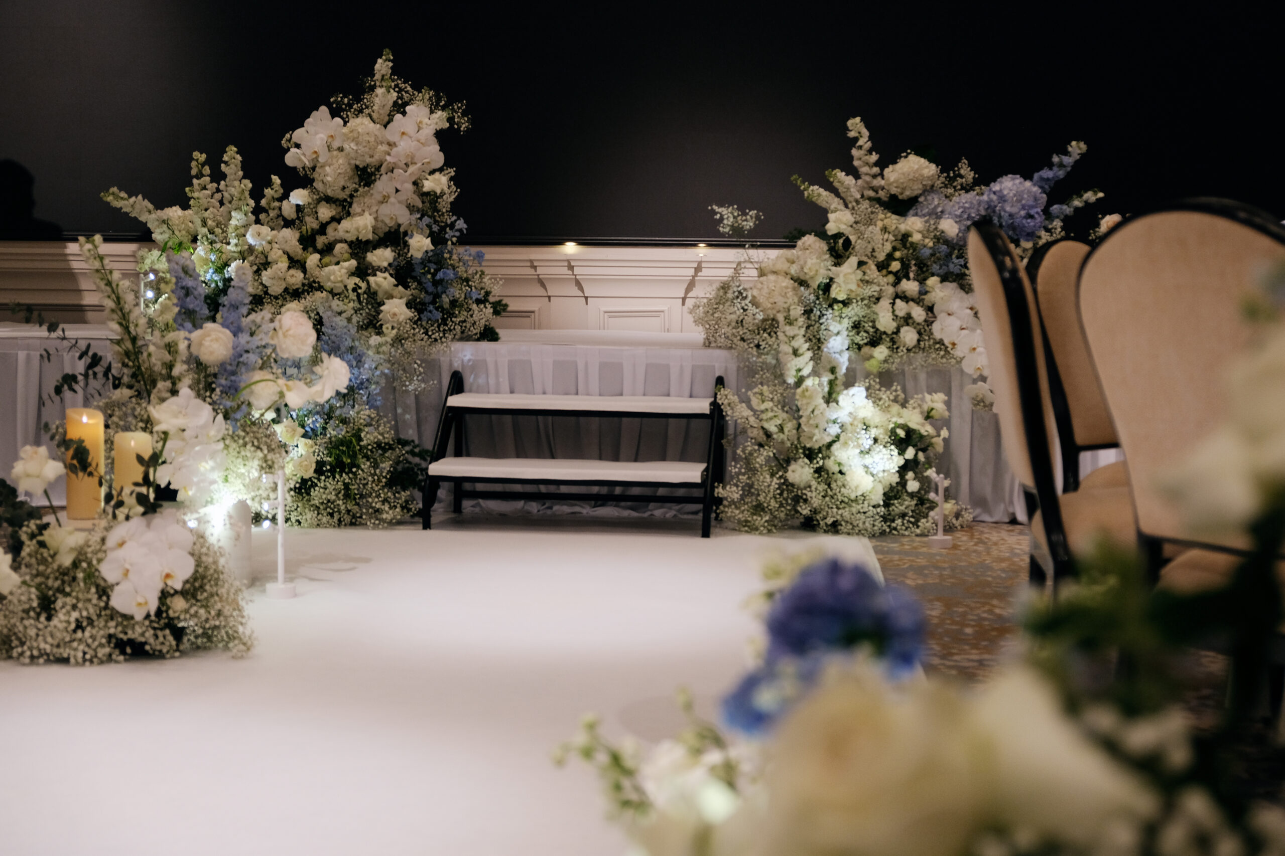 A beautifully decorated stage with white floral on the sides of the stairs, with soft lighting, and neutral-toned seating at Raffles Hotel Singapore.