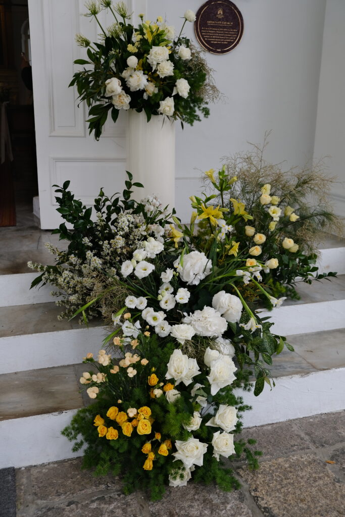 Elegant white and yellow floral arrangements, consisting of roses, creamy lisianthus, delicate spray carnations, and bright alstroemeria, decorated the steps leading up to a church entrance, suggesting a wedding ceremony at the Armenian Church Singapore.