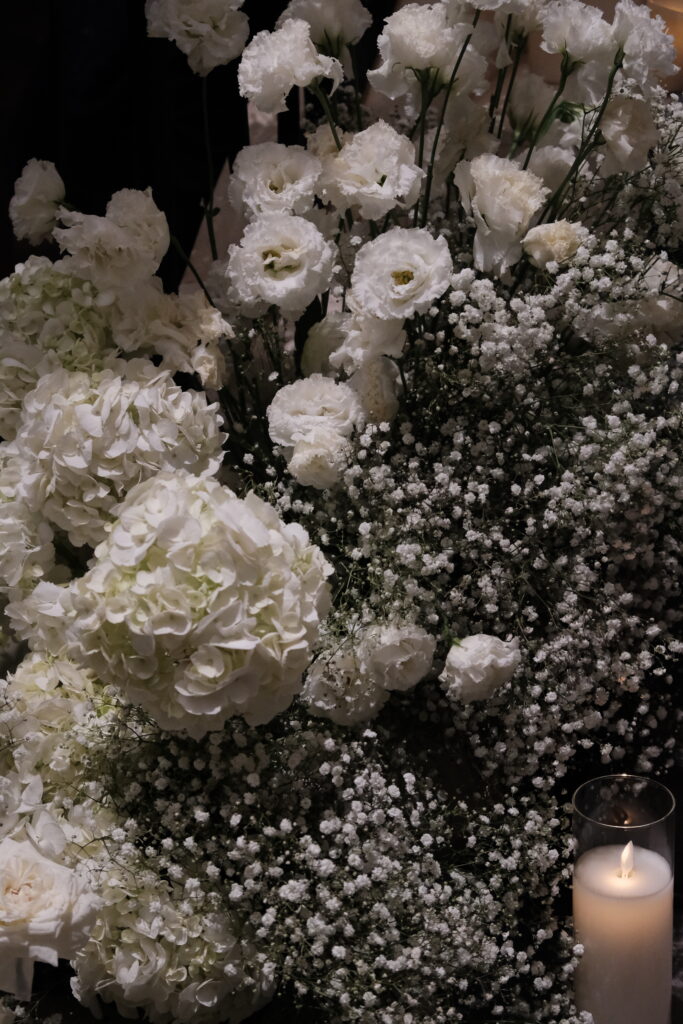 A close-up of a dense arrangement of white roses, hydrangeas and delicate baby's breath, interspersed with glowing candles, decorating a staircase for a luxury wedding at Caroline Mansion Singapore.