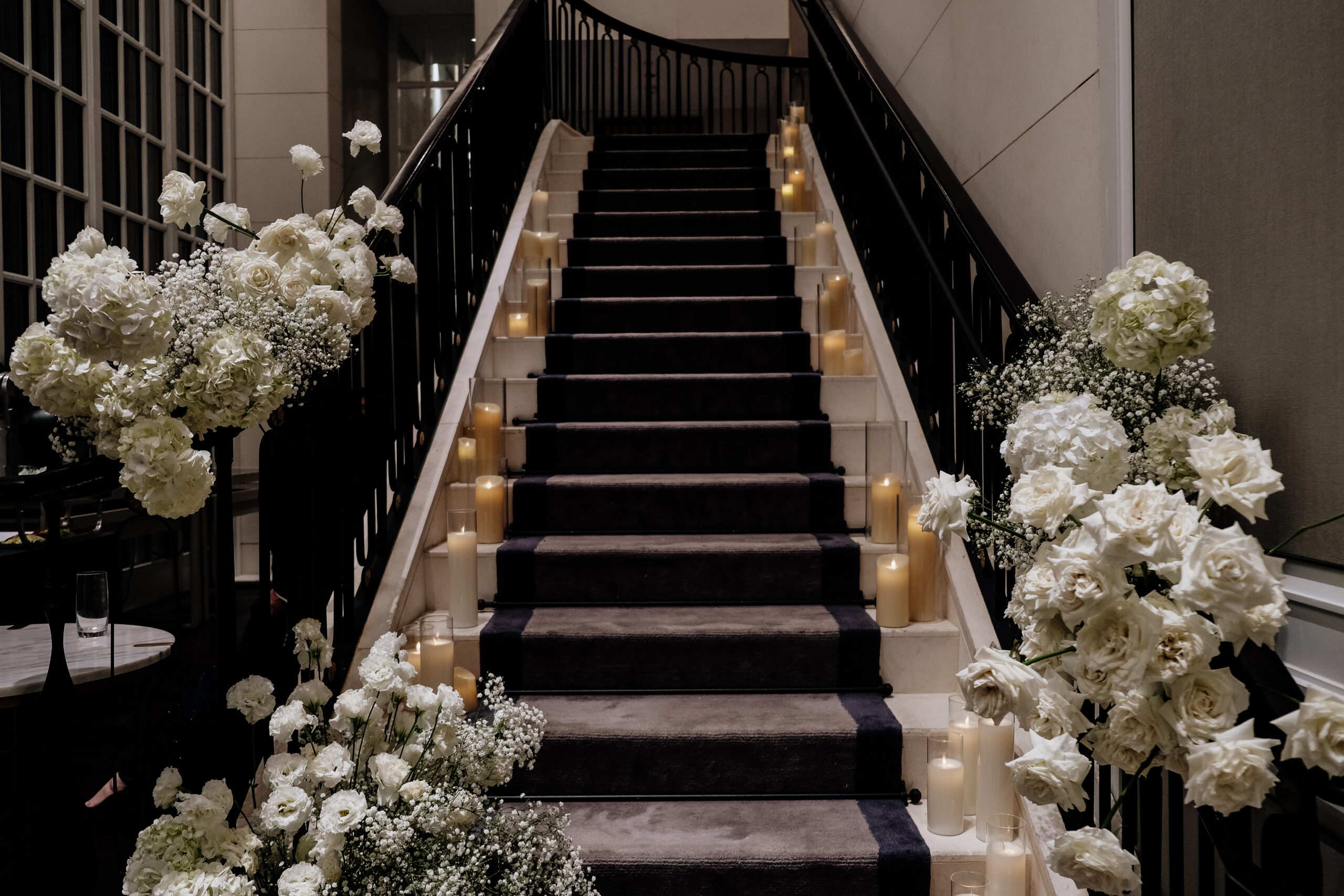 A grand staircase adorned with lush white floral arrangements and glowing candles, creating an elegant ambiance for a wedding at Caroline Mansion Singapore