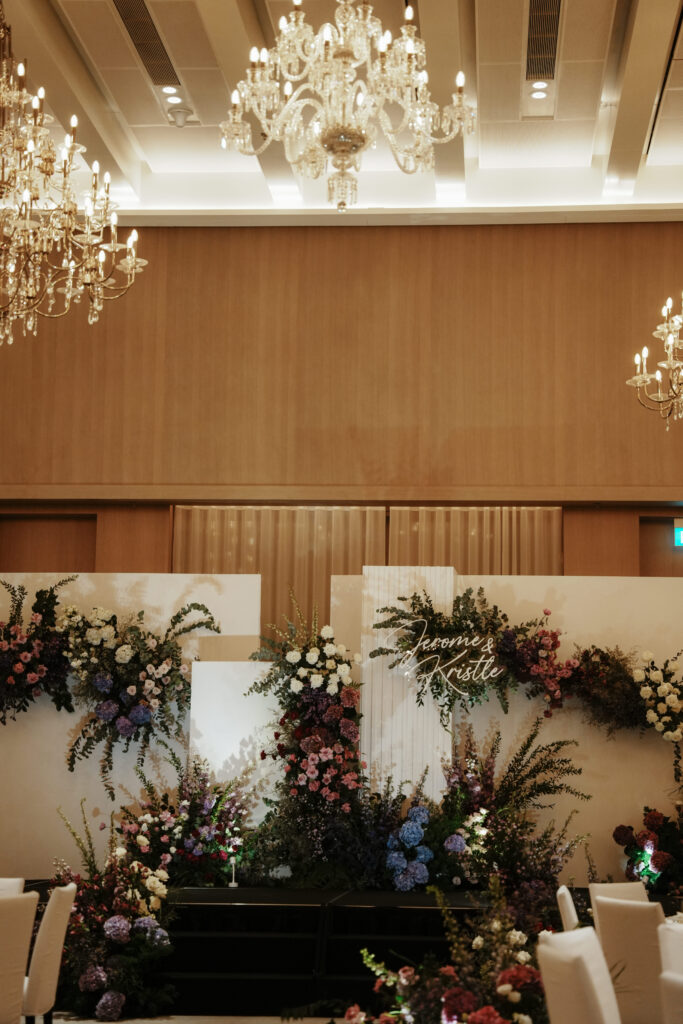 Ballroom overview with purple theme floral installations under crystal chandeliers.