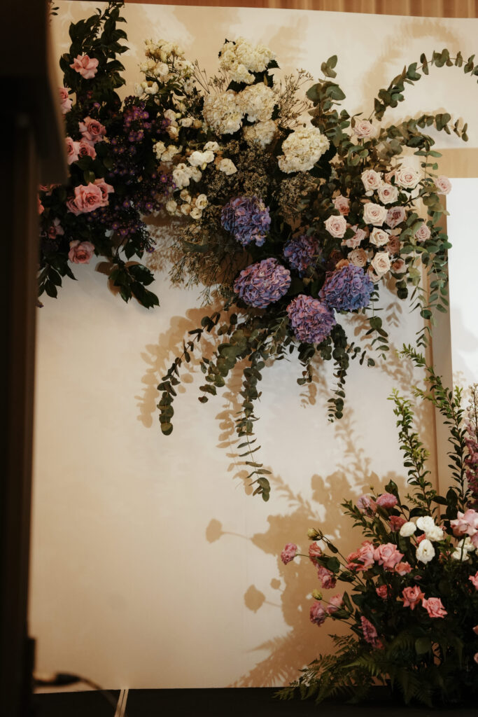 Floral installation cascading over modern white panels with soft white, violet roses and hydrangeas.
