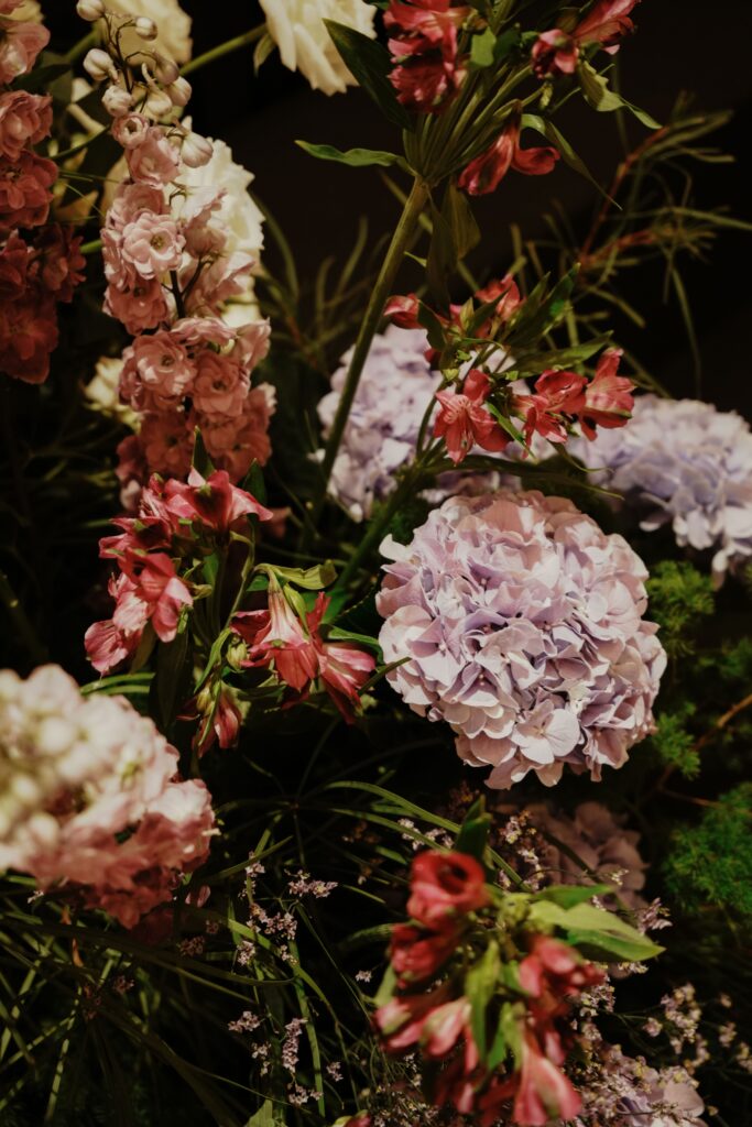 Close-up of purple hydrangea accented with red and mauve florals and greenery.