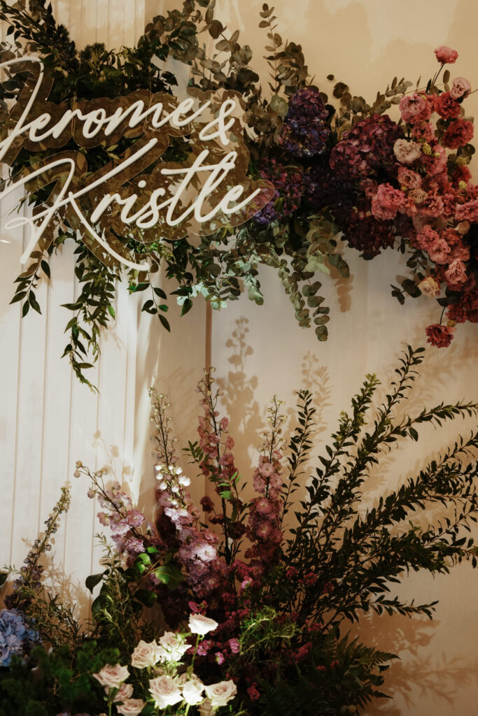 Floral overhead for the backdrop with mauve and burgundy flowers framing the couple’s name sign