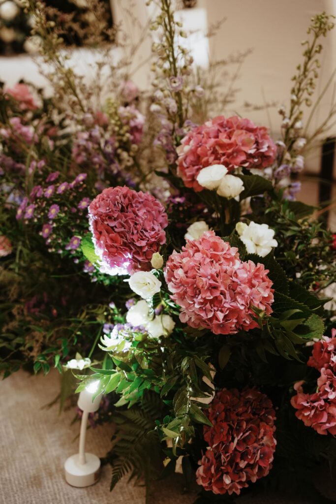 Lush low arrangement of bold purple hydrangeas with deep green foliage for the aisle.