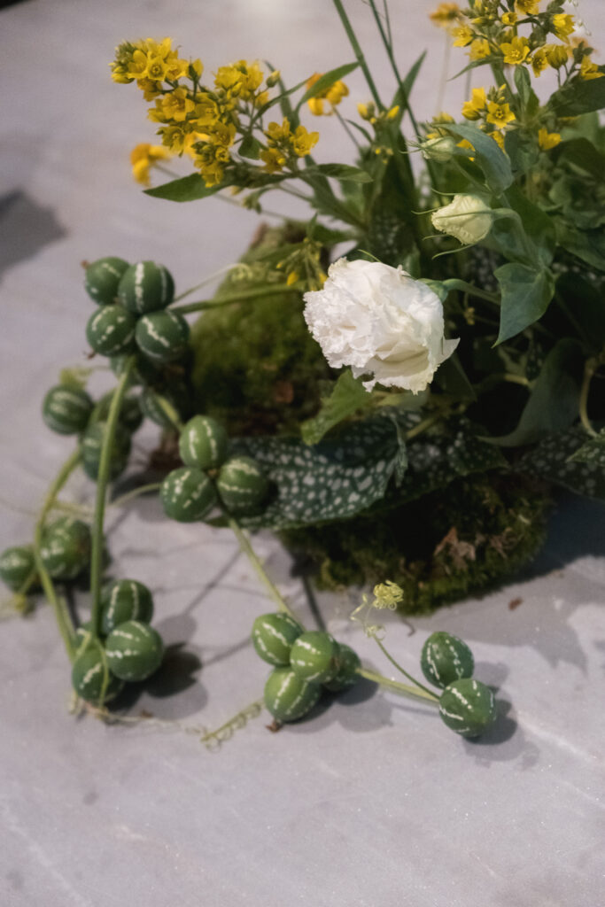 Close up of an unstructured floral design with hops, yellow blooms, white carnations and cucumelon vines for wild tablescape style at Open Farm Community.