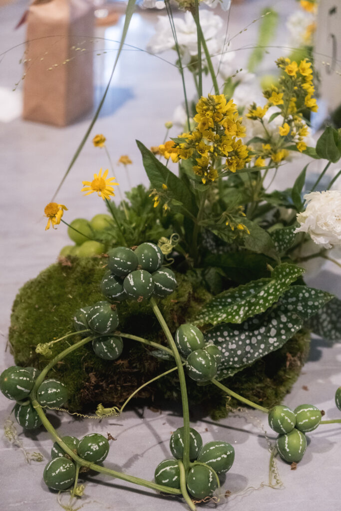 A wild and foraged-style centerpiece featuring unruly vines and loosely arranged greens, echoing a freshly gathered nature look at Open Farm Community.
