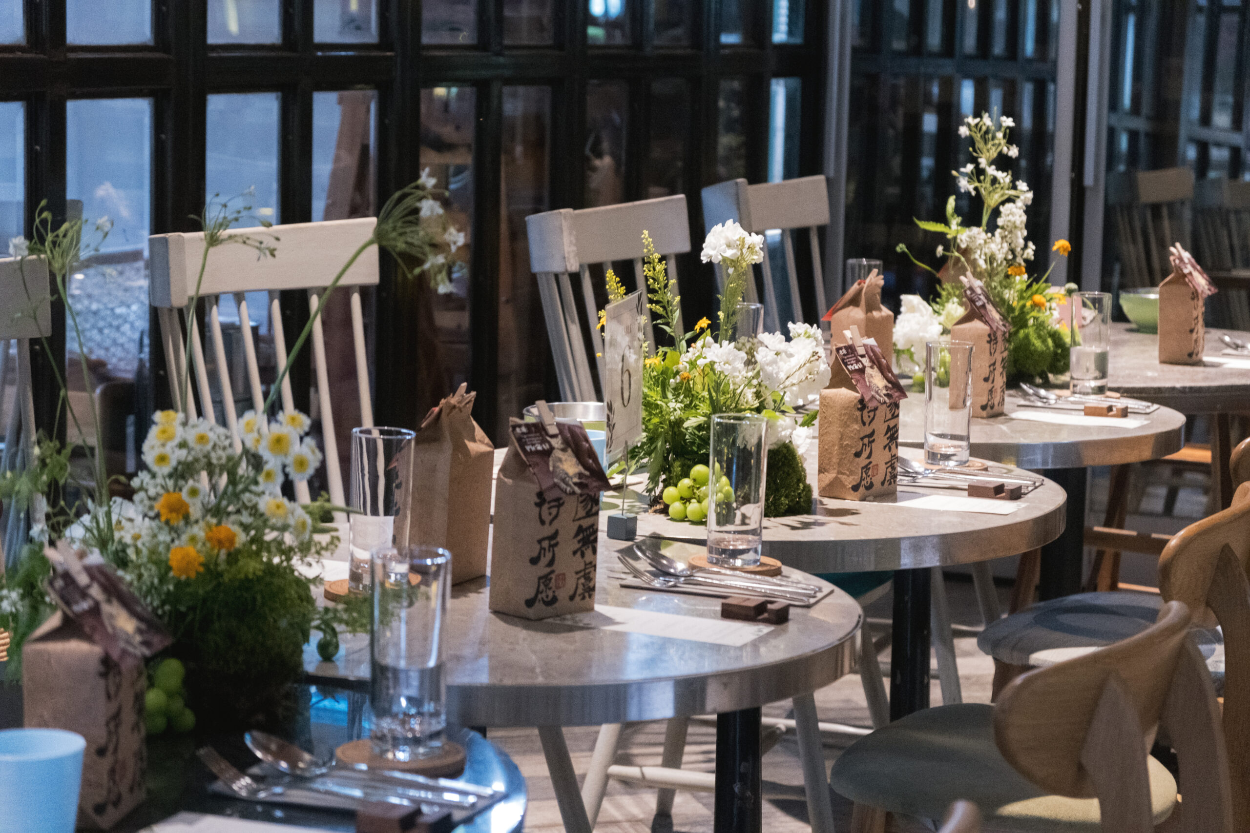 Rustic wedding tablescape with white chairs, floral centerpieces, and brown gift bags at Open Farm Community