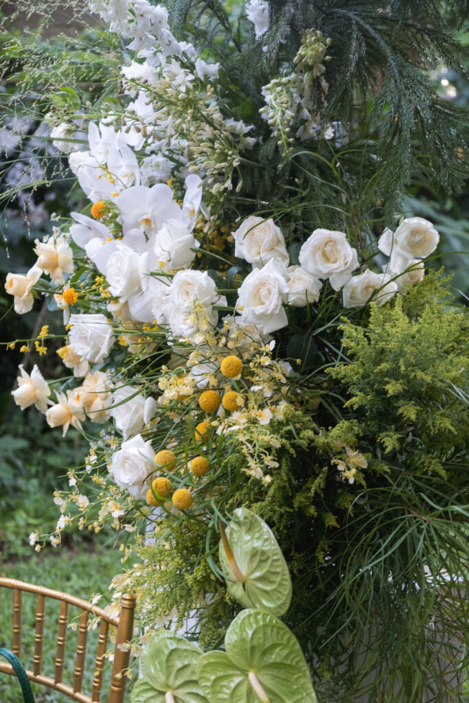 Lush floral installation with white roses, orchids, yellow billy balls, and cascading greenery outdoors