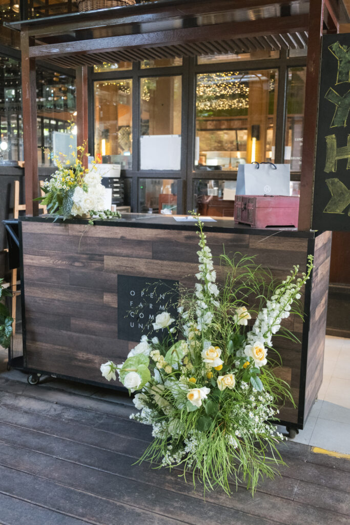 Lush floral installation with white roses, orchids, yellow billy balls, and cascading greenery outdoors