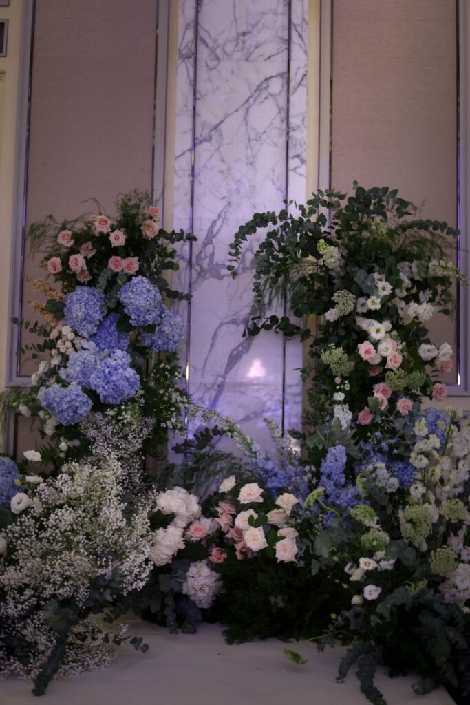 Floral installation with layered garden-style arrangements framing a ceremonial backdrop in soft pastel tones, Shangri-La Singapore