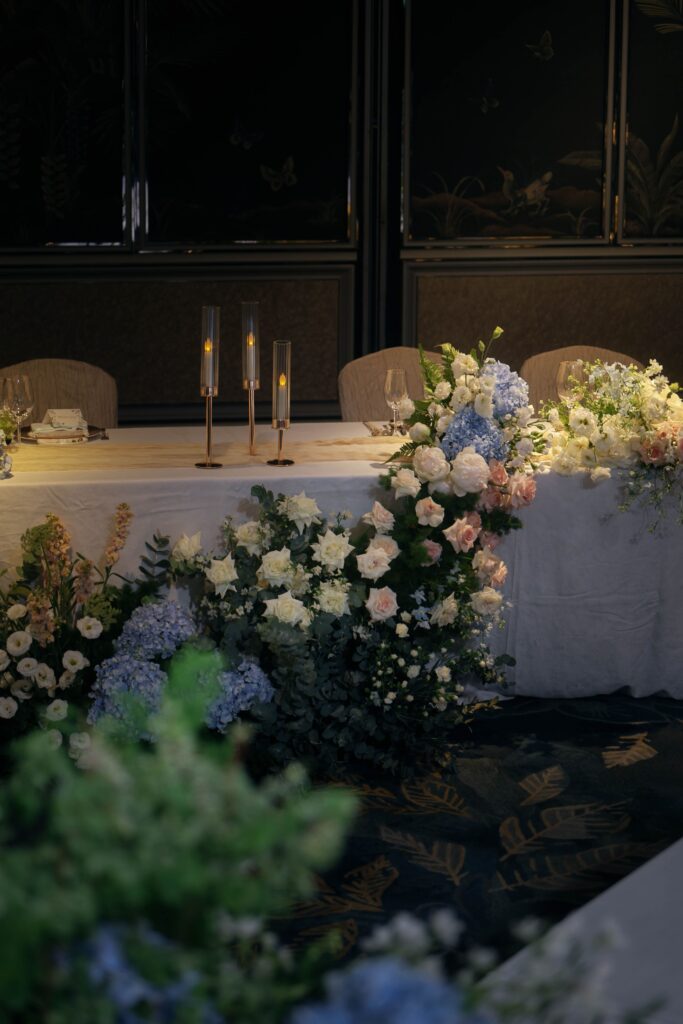 Long VIP table styled with refined low floral arrangements and soft candle accents in a ballroom wedding, Shangri-La Singapore