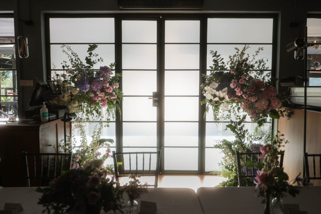 Floral styling framing frosted glass panels to create privacy for a glass venue wedding entrance at The Blackbird, Singapore
