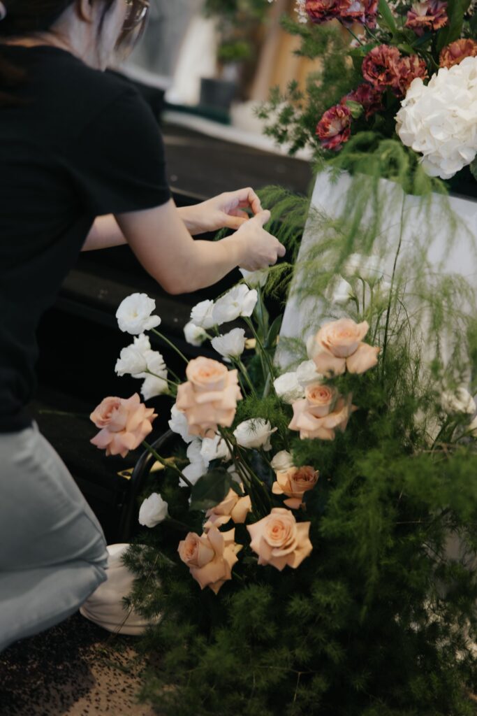 Florist arranging roses and carnations in textured wild organic composition for wedding stage at Andaz Singapore