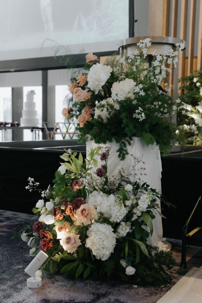 Floral arrangement on pedestal at stage steps featuring roses, greenery and antique garden styling at Andaz Singapore