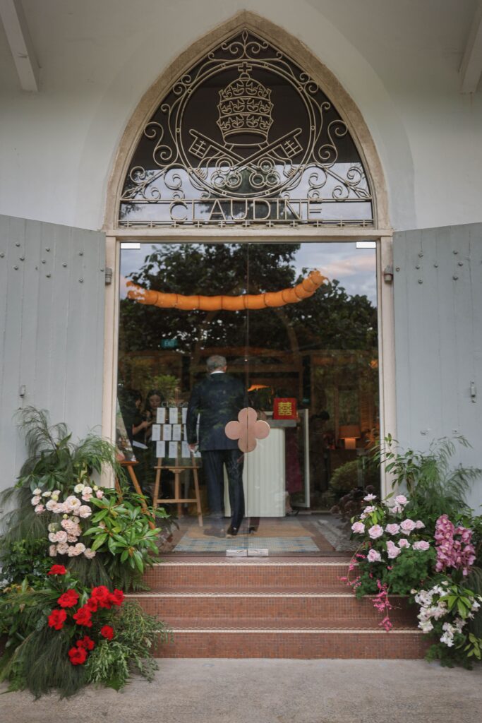 Frontal view of arched venue entrance framed with organic white, pink and red floral installations for a modern wedding celebration, Claudine Singapore