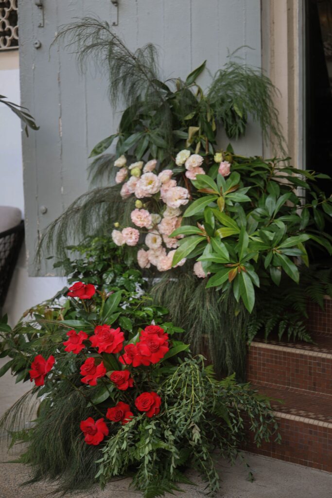Close-up of pink camellias and red roses with textured greenery arranged in a modern organic style at the venue entrance, Claudine Singapore