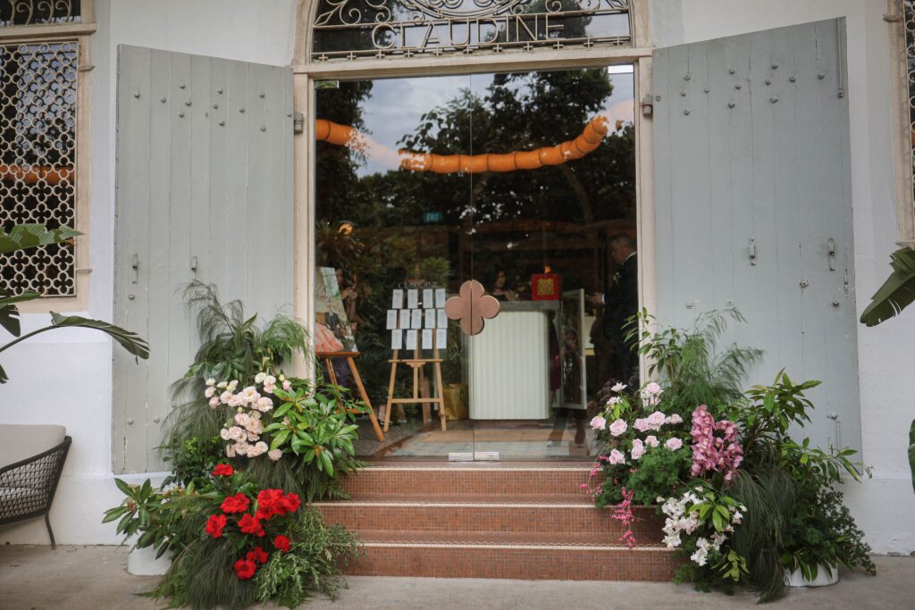 Organic entrance floral installation with white blooms, pink, red roses, pink orchids and abundant greenery flanking the venue steps, Claudine Singapore