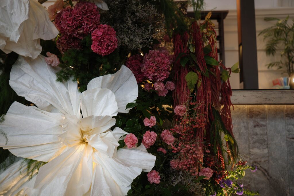 Detailed view of the bar backdrop featuring white paper flowers, blue hydrangea, pink florals, and lush greenery arranged vertically, Empress Restaurant Singapore