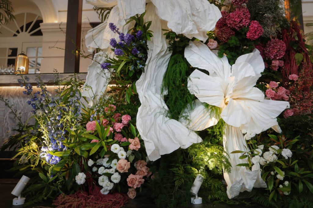 Sculptural floral backdrop with fresh white blooms, blue hydrangea, pink florals, layered greenery, and large white paper flowers arranged vertically over the bar, Empress Restaurant Singapore