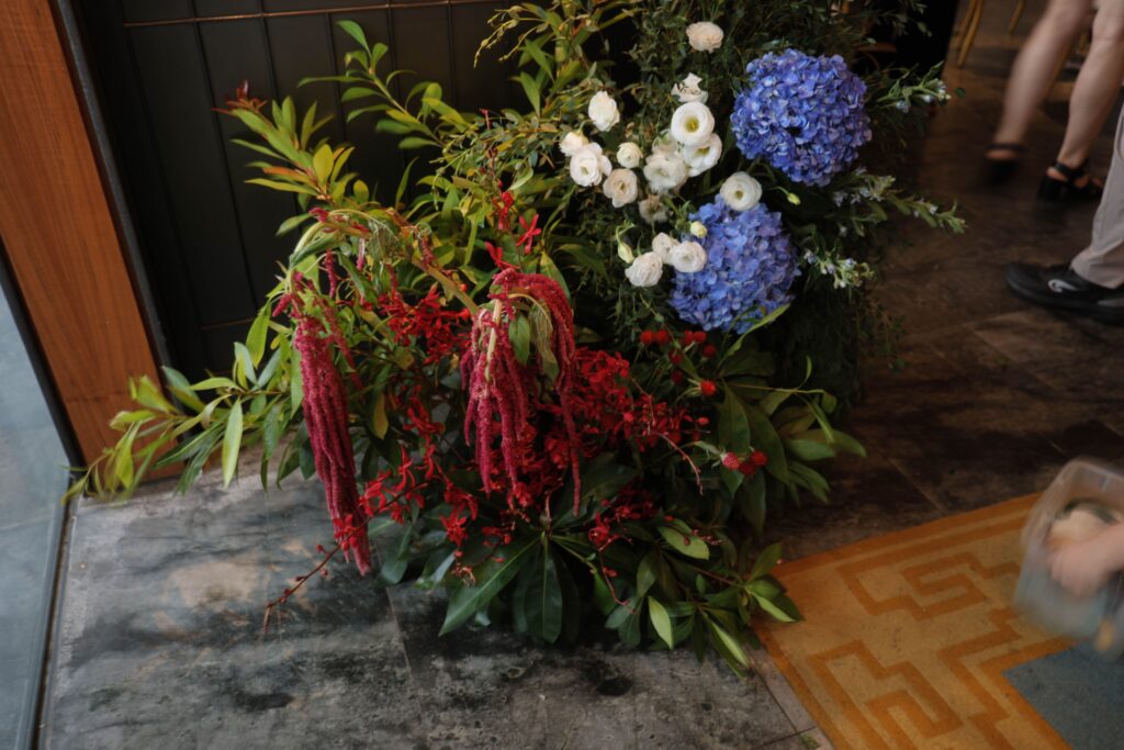 Entrance floral arrangement with lush greenery, blue hydrangea, white blooms, and cascading red elements styled at floor level near the restaurant entrance, Empress Restaurant Singapore
