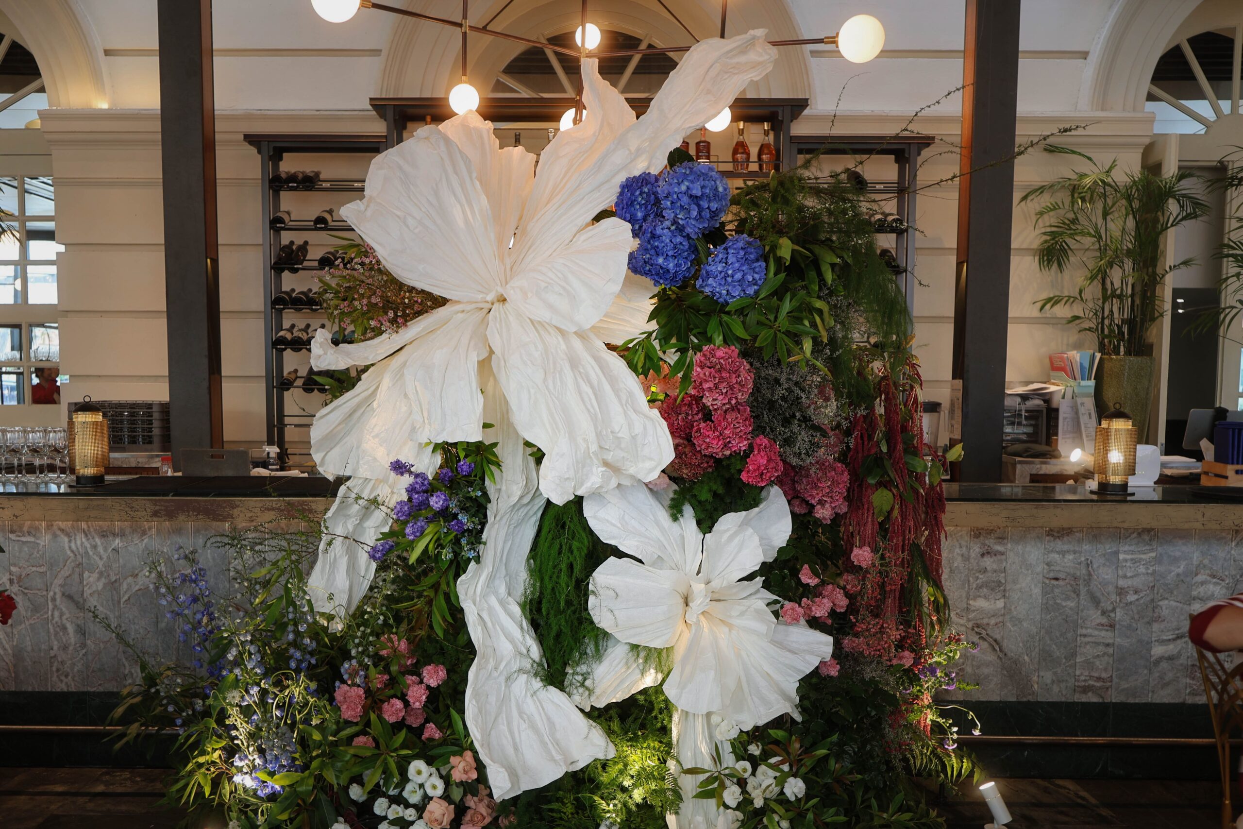 Full view of the floral backdrop over the restaurant bar featuring fresh flowers, greenery, and large white paper flowers as the main focal point, Empress Restaurant Singapore