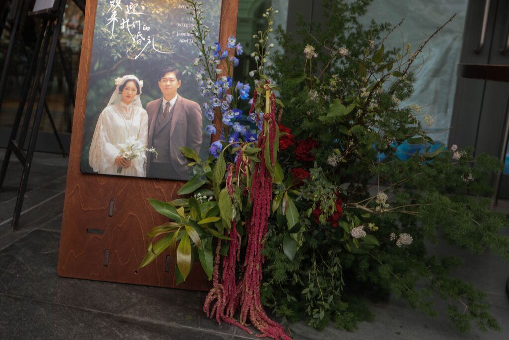 Wedding welcome sign styled with fresh florals, greenery, blue and white flowers, and cascading red elements placed outside the restaurant entrance, Empress Restaurant Singapore