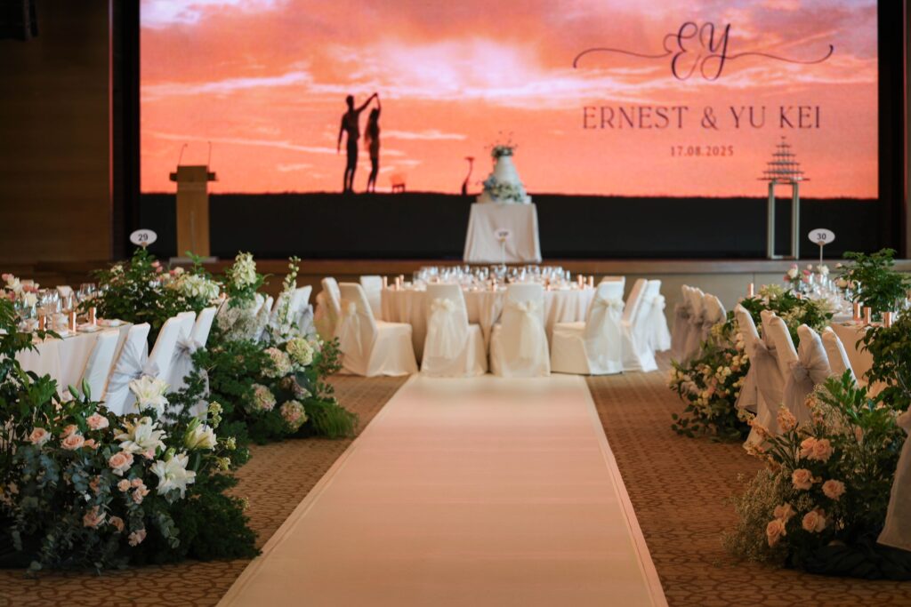 Garden-inspired ballroom ceremony setup with lush aisle florals in white hydrangeas, blush roses and layered greenery framing the stage at The Ritz-Carlton Singapore