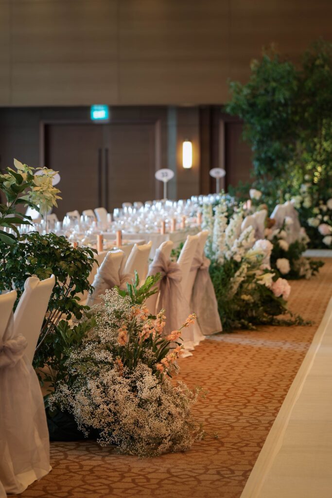 Long ceremony aisle lined with lush garden-style floral clusters in white and blush tones at The Ritz-Carlton Singapore