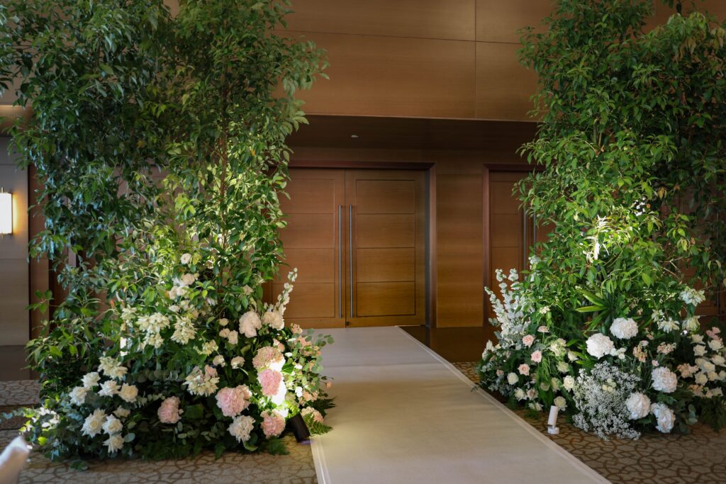 Foyer entrance framed with tall greenery trees and layered white floral arrangements forming a welcoming garden transition at The Ritz-Carlton Singapore