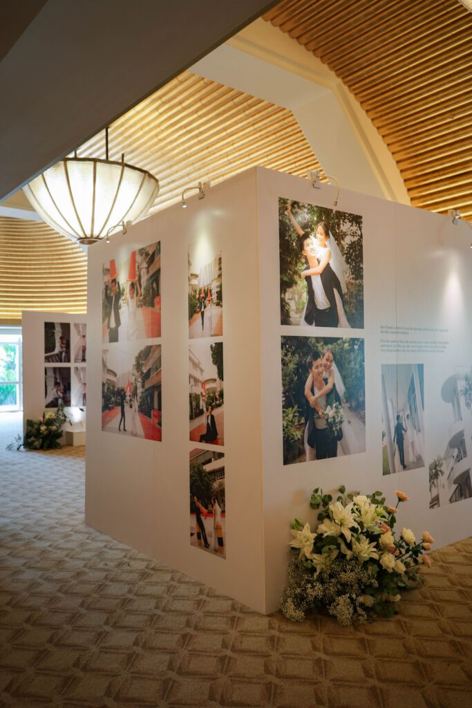 Wedding photo exhibition wall displaying milestone images styled with soft floral arrangements as part of a memory lane concept at The Ritz-Carlton Singapore