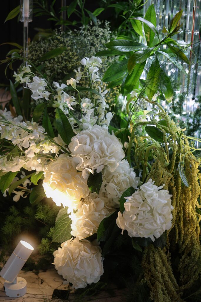Close up of white hydrangeas and orchids paired with cascading green amaranthus and lush foliage arranged in a garden inspired floral cluster for a romantic ballroom wedding at JW Marriott Hotel Singapore