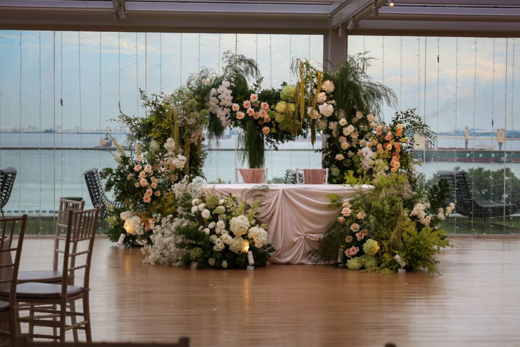 Wide view of asymmetrical floral ceremony installation with greenery, blush roses, orchids, lisianthus and hydrangeas framing the couple’s stage while keeping the sea view visible at Sky Garden Sentosa, Sentosa Singapore