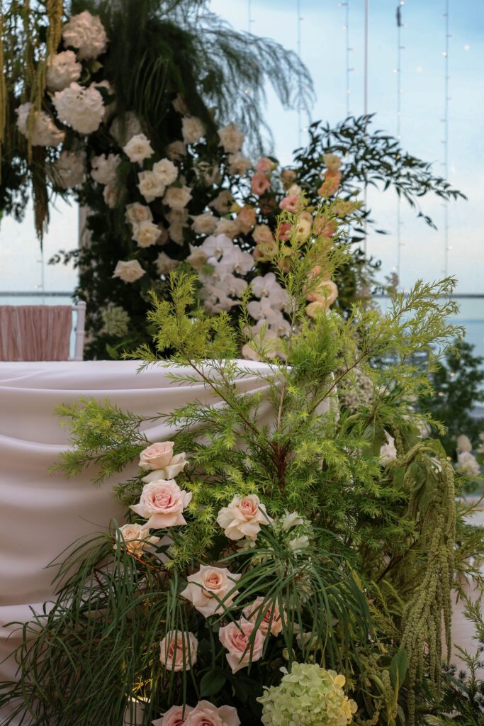 Asymmetrical floral installation with garden greenery, blush roses, white hydrangeas, orchids, lisianthus and cascading foliage framing the ceremony stage at Sky Garden Sentosa, Sentosa Singapore