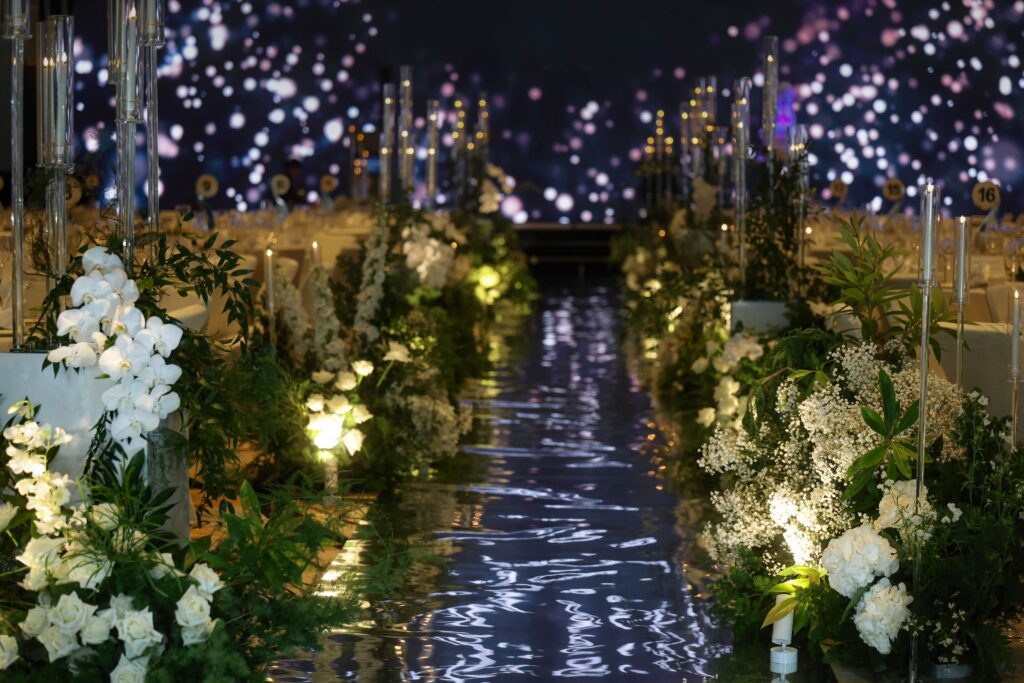 Long wedding aisle lined with white and green florals and layered candles creating a warm and immersive pathway towards the stage at JW Marriott Hotel Singapore South Beach