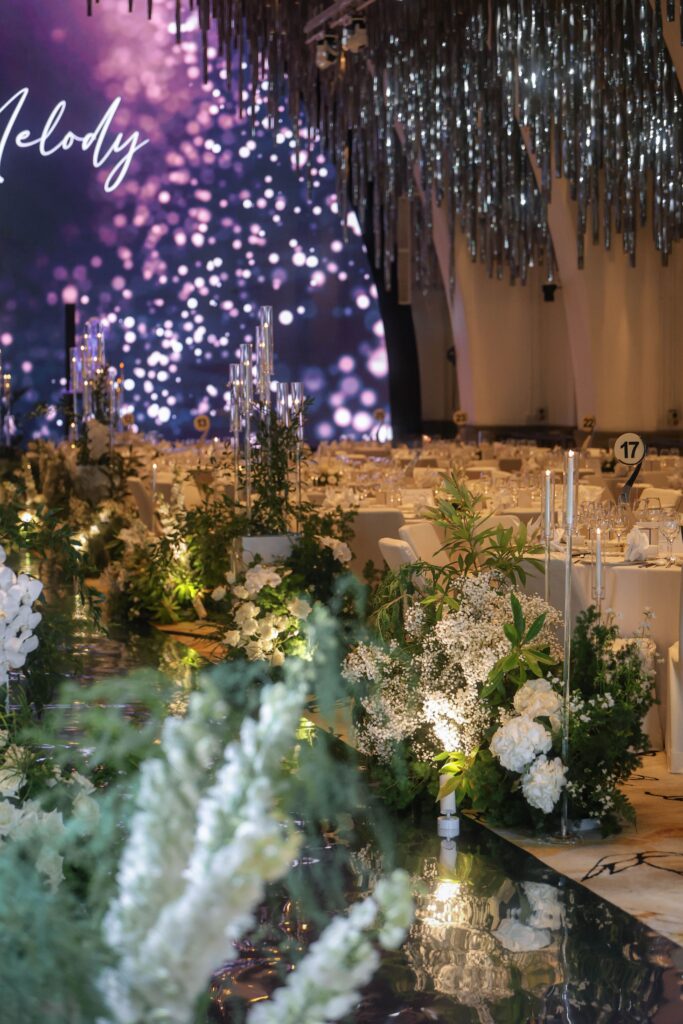 Low white and green floral arrangements paired with candles along a reflective aisle creating warmth and continuity at JW Marriott Hotel Singapore South Beach