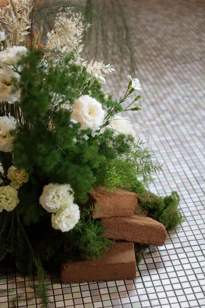 Grounded floral arrangement with white carnations, soft greenery, and natural wood layers designed with warm earthy elegance at Min Jiang at Dempsey, Singapore