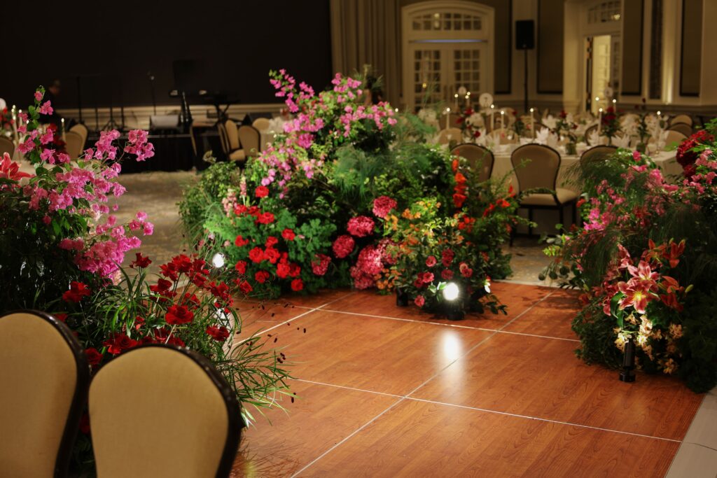 Vibrant bougainvillea-inspired floral arrangements with pink and red tones, roses, and layered greenery forming an English garden style around the dance floor at Raffles Hotel Singapore