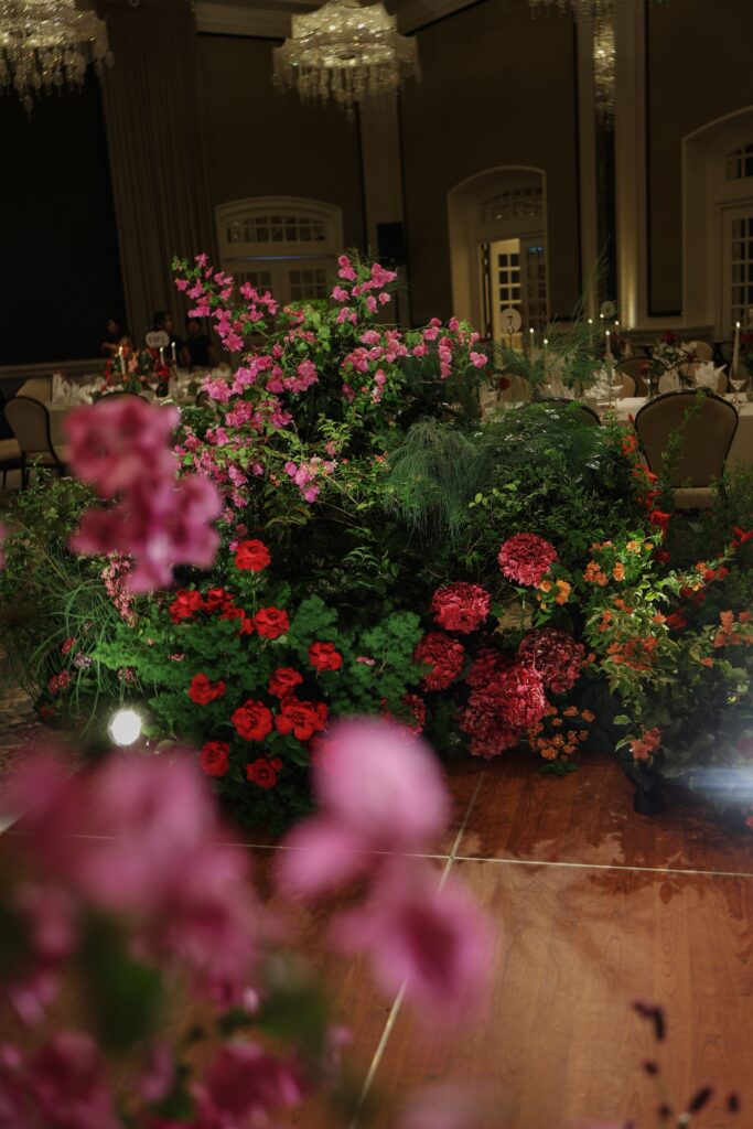 Close-up of bold pink and red floral mix with roses, bougainvillea-inspired textures, and dense greenery in an English garden style at Raffles Hotel Singapore
