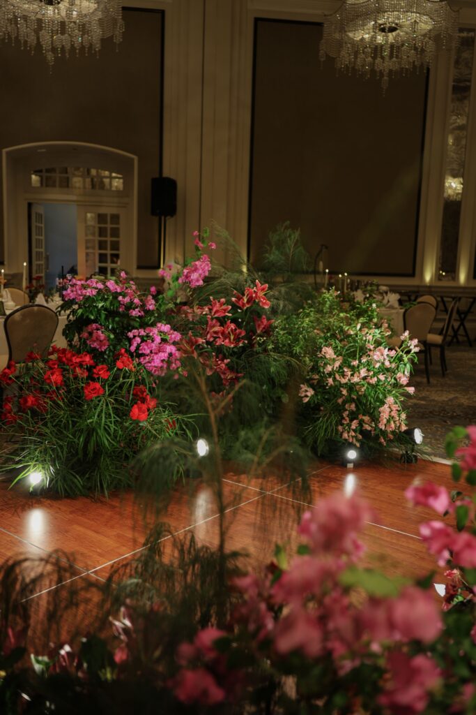 Layered floral arrangements with bougainvillea tones, roses, and lush greenery creating depth and a full garden look surrounding the dance floor at Raffles Hotel Singapore