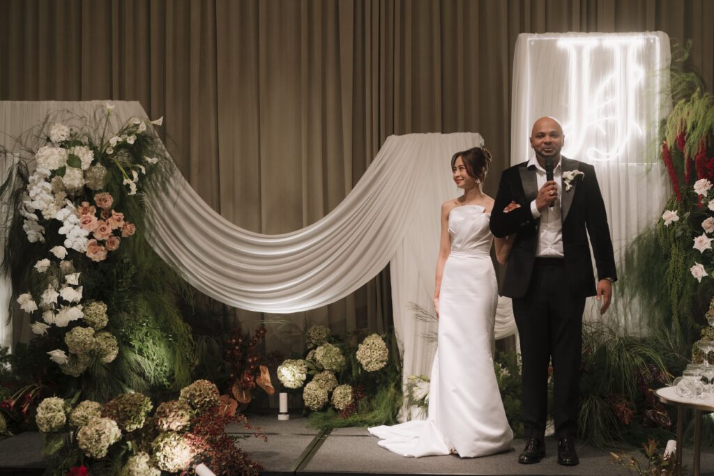 Modern classic ballroom wedding stage with soft drapery backdrop, sculptural floral installations, and romantic layered styling for an elegant reception at Raffles Hotel Singapore